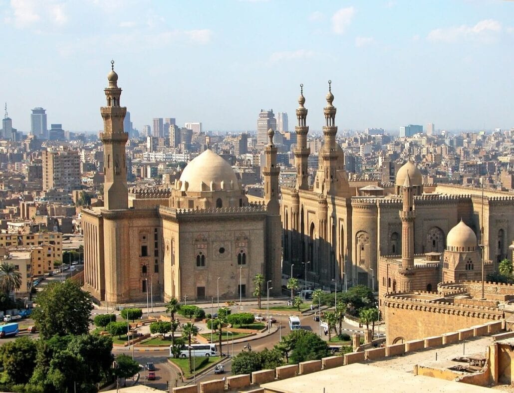 A breathtaking aerial view of Cairo reveals the iconic Sultan Hassan Mosque and Al-Rifa'i Mosque prominently in the foreground. This cityscape, dotted with historic minarets and modern structures under a clear blue sky, is truly a bucket list destination for any traveler.