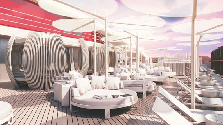 Outdoor lounge area with circular white cushioned seating, large canopies, and modern architectural elements, including wooden structures and large white circular shade disks. The decking is wooden, and the sky is pinkish—reminiscent of the stylish design found on Virgin Voyages’ first cruise ship.
