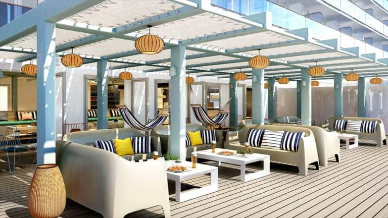 An outdoor lounge area with modern seating arrangements, including white cushioned sofas, striped pillows, and white tables set on a wooden floor. Overhead, pergolas with hanging lanterns create a cozy ambiance unique to Virgin's eateries. Hammocks are suspended between some pergola posts.