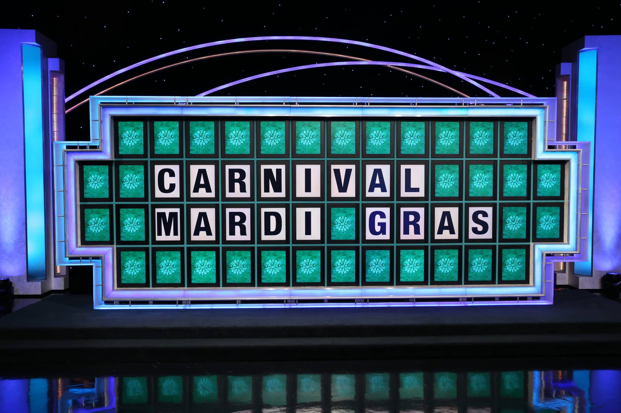 A game show board displays the solved puzzle phrase "CARNIVAL MARDI GRAS" in white letters on green tiles. The board, glowing with blue and purple lights, and set against a starry black background, evokes the excitement of a New Ship from Carnival Cruise Line.