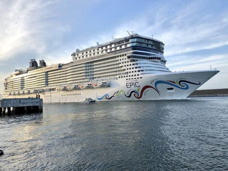 A large cruise ship named "Epic" is docked at the San Juan pier. The ship has multiple decks and is adorned with colorful wave designs on its hull. The sky is clear, and the water around the ship is calm.
