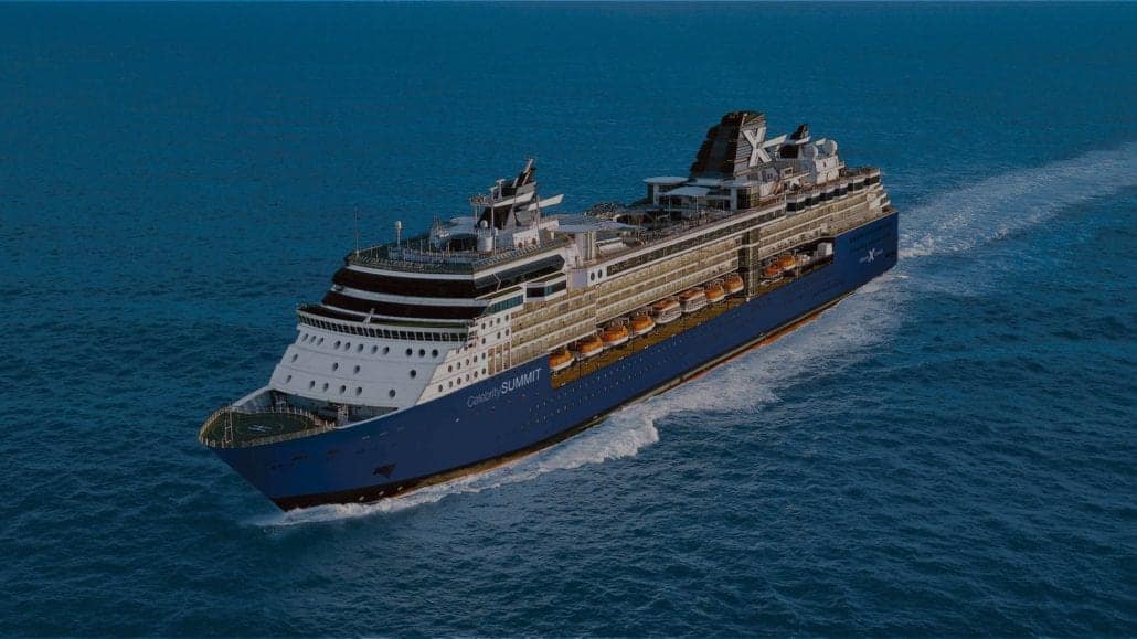 A large cruise ship sails through the ocean under a clear blue sky. The vessel is predominantly white with dark accents and has multiple decks, lifeboats, and a distinctive, large smokestack. Waves trail behind as it moves forward.