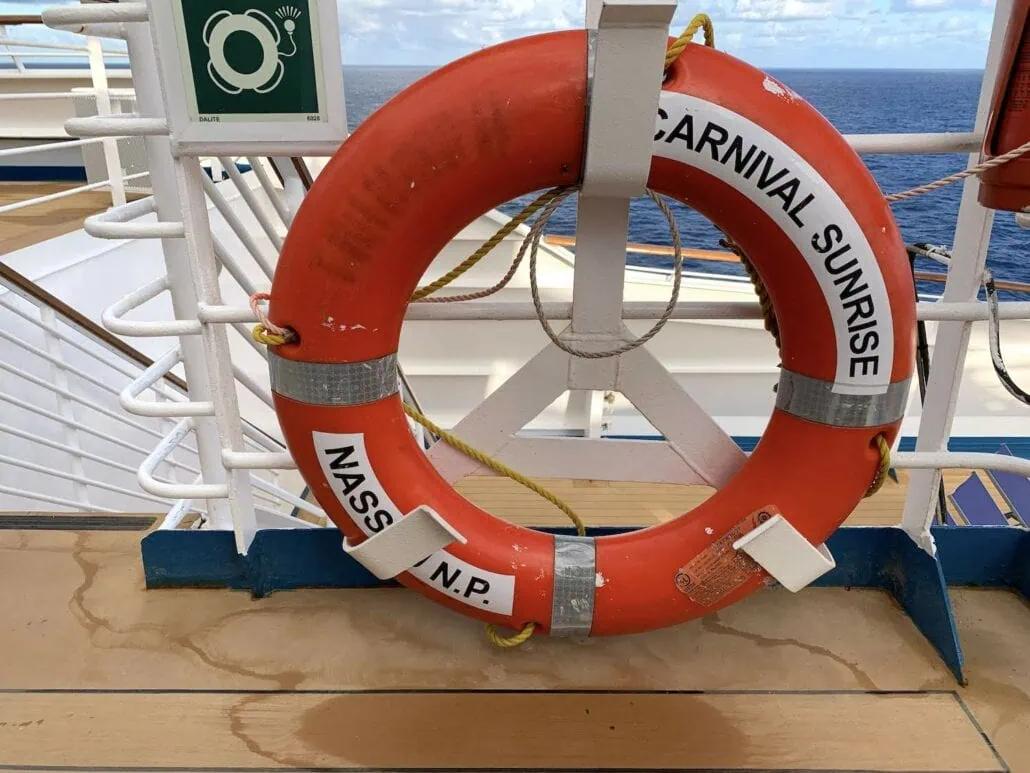An orange life preserver labeled "Carnival Sunrise" and "Nassau, N.P." hangs on the cruise ship's deck railing, echoing the 2019 upgrades in its design as the expansive ocean stretches out in the background.