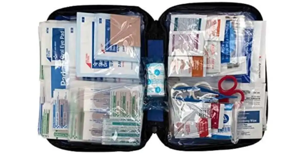 An open first aid kit, ideal for what every girl should pack, reveals various medical supplies like adhesive bandages, gauze pads, and antiseptic wipes. Scissors and adhesive tape are neatly organized in transparent pockets within the sleek black case.