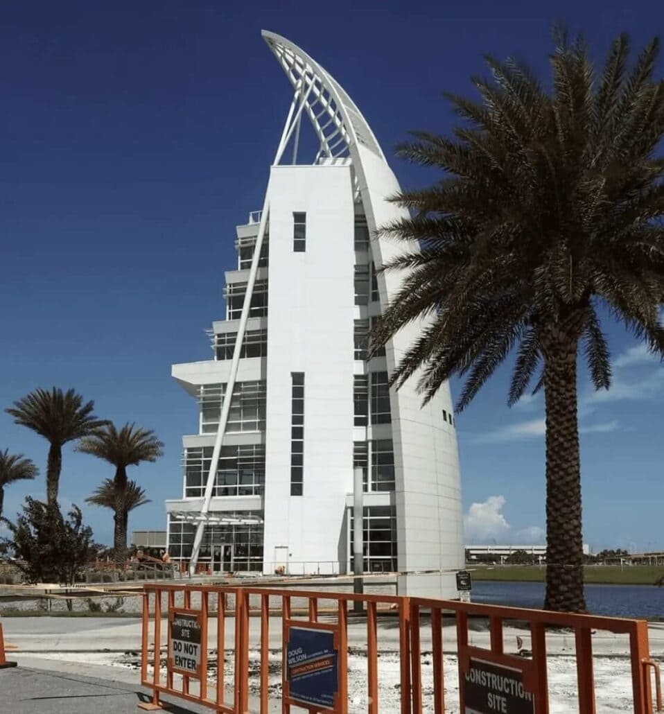A modern white building with a sail-like design is under construction, surrounded by palm trees and caution signs in front of a blue sky. If you're cruising from Port Canaveral, be sure to check out this architectural marvel for a glimpse of the expert tips in innovative design.