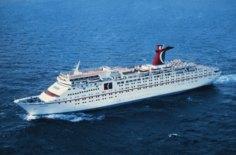 A large white Carnival Cruise Line ship sails on the ocean, celebrating 25 years. The vessel has multiple decks, lifeboats visible on the sides, and a distinctive red and black funnel adorned with a logo at the top. Decorative flags from front to back add to its charm as it departs from Tampa.