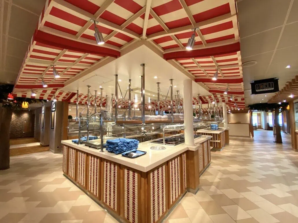 A cafeteria-style buffet aboard the Carnival Panorama features a red and white striped ceiling. Multiple serving stations with empty trays and utensils await guests. The tiled flooring complements stacks of blue napkins on the counters. This well-lit space, perfect for a ship review, is currently unoccupied.