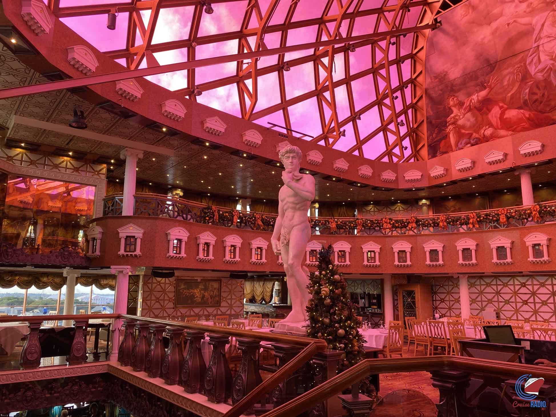 Interior of a the steakhouse dining area on the Carnival Pride with a classical statue of David as a centerpiece under a pink-tinted skylight.