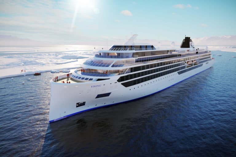 A large white cruise ship sails through calm waters on the Great Lakes Route, with ice and snow-covered land in the background. The vessel's name "VIKING" is visible on the side, and there are clear skies overhead. A few small boats and people can be seen near the ice, highlighting Viking Cruises' 2023 adventures.