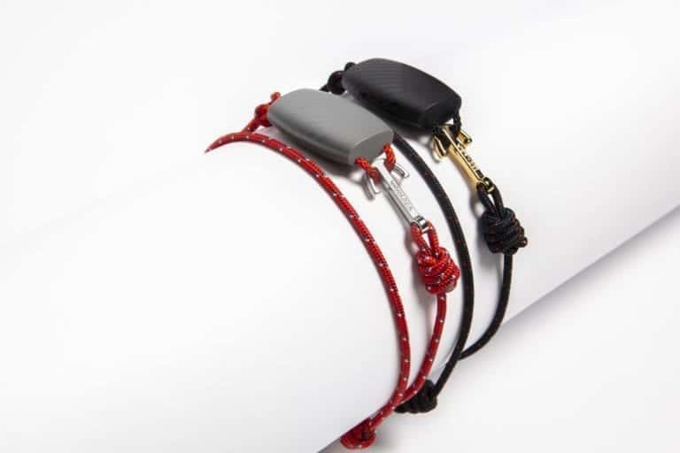 Three coiled bracelets are displayed on a white surface. One is black with a black clasp, another is red with white dots and a gray clasp, and the third resembles a stylish wearable device with a red and black twisted cord and a metallic clasp, perfect for your next Virgin Voyages adventure.