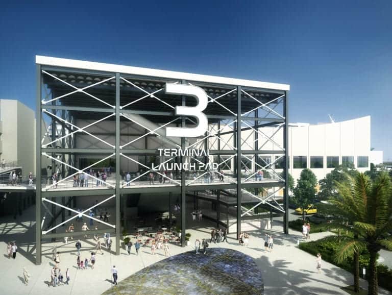 A large modern building with a prominent sign reading "TERMINAL LAUNCH PAD 3" takes shape. The structure features a steel framework and open spaces, with people walking and gathering outside. There's a pathway and landscaped area with trees and greenery in the foreground, evoking Port Canaveral's new cruise terminal vibe.