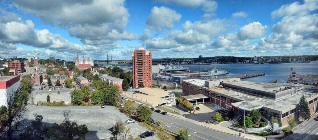 A panoramic view of Halifax Cruise Port reveals a waterfront cityscape with a mix of residential and commercial buildings. A bridge looms in the background, while docked ships line the shoreline beneath a partly cloudy sky, offering endless ideas for what to do in this vibrant locale.