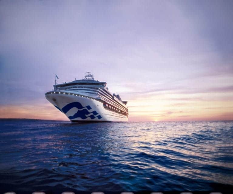 A large cruise ship sails on calm waters during a sunset, with the sky displaying hues of pink and orange. The ship features multiple decks and a distinctive wave-like design on its hull.