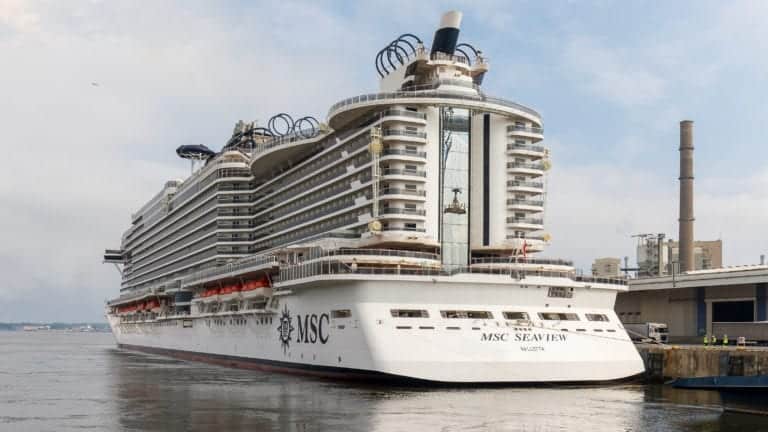 A large MSC Seaside-class ship named "MSC Seaview" is docked at a port, ready to resume voyages. The ship boasts multiple decks with balconies and a pristine white exterior. The name "MSC Seaview" and "Valletta" are visible on the stern, with several lifeboats attached along the side.