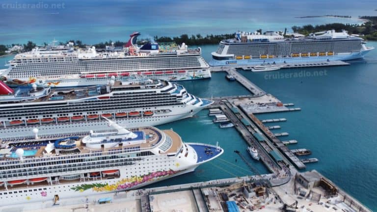 Aerial view of cruise ships docked at a bustling port with turquoise water. The port is alive with piers reaching into the sea, and a construction site stands in the foreground, hinting at future shore excursion possibilities as CDC restrictions ease.