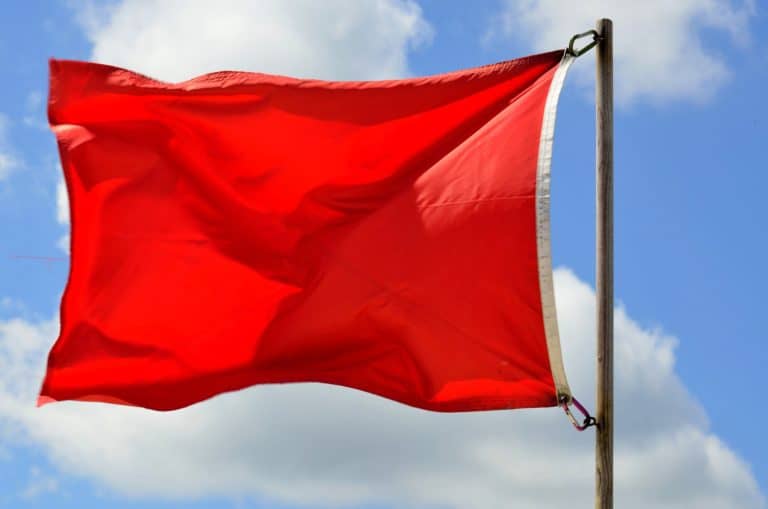 A red flag is attached to a wooden pole and flutters against a backdrop of a blue sky with scattered clouds, signaling caution as Hurricane Ian approaches.
