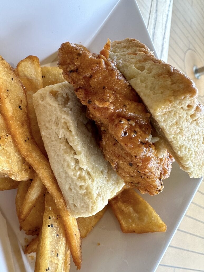 A crispy fried chicken breast is expertly sandwiched between two halves of a biscuit, reminiscent of flavors enjoyed on a Carnival Radiance cruise. The plate also features perfectly seasoned potato wedges, offering a delightful taste that hints at well-loved culinary tips and tricks.