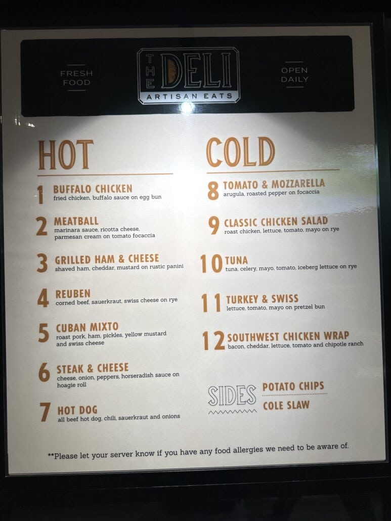 The Deli Artisan Eats" menu board on the Carnival Radiance features an array of delectable hot and cold sandwiches, numbered 1 to 12. Enjoy creations like Buffalo Chicken, Meatball, and Turkey & Swiss. Sides include crispy potato chips and creamy coleslaw. Don't miss our tips on food allergies!