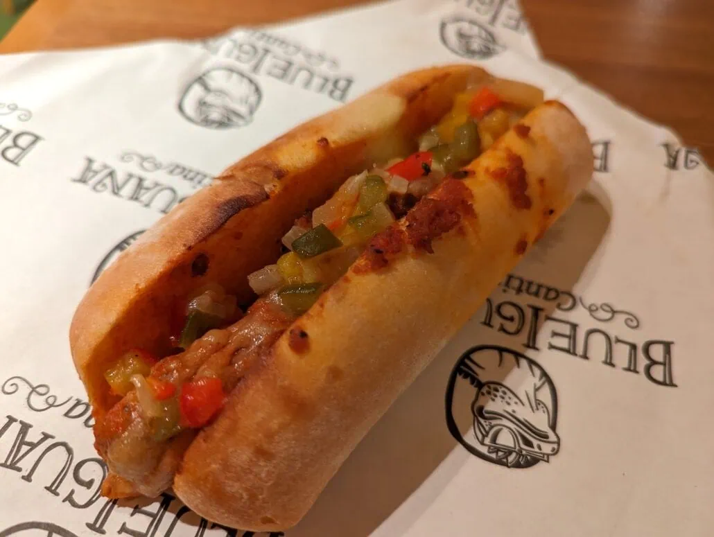 A grilled sandwich on branded paper, reminiscent of Carnival Venezia Dining, filled with meat, chopped pickles, and peppers, all encased in a crispy, toasted bun.