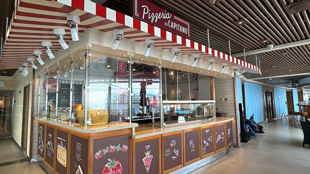 Pizzeria del Capitano, a charming spot reminiscent of Carnival Venezia dining, boasts a red and white striped awning and glass windows. Inside, the wooden decor and hanging lights offer a warm ambiance, with promotional signs and a menu board at the counter enhancing its inviting appeal.