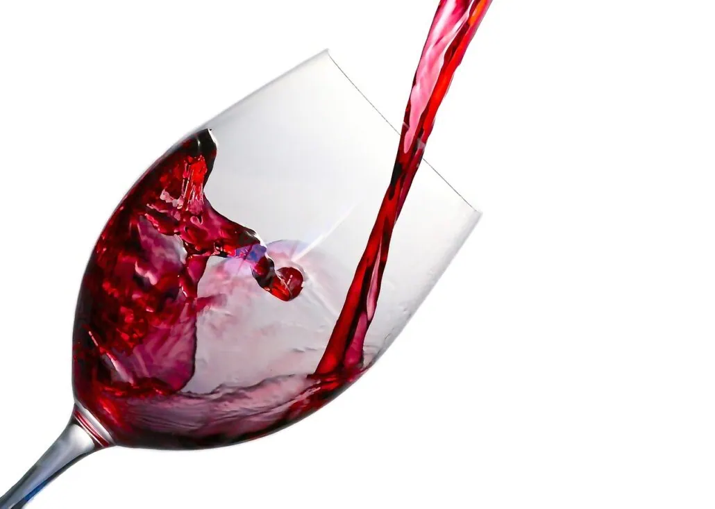 Red wine being poured into a tilted wine glass against a white background evokes the elegance of Carnival Venezia dining. The splashes inside the glass capture the vibrant essence of an unforgettable culinary journey.