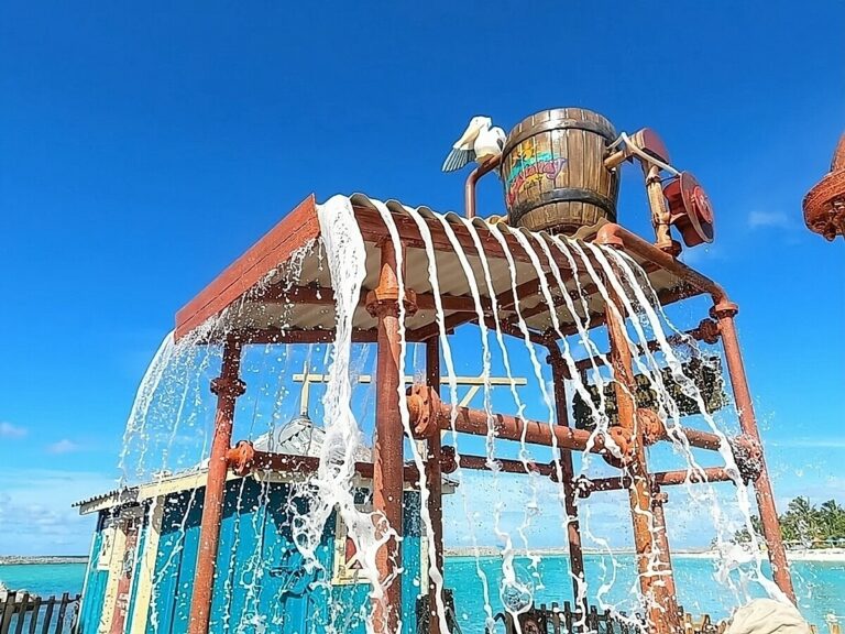 A wooden barrel apparatus pours water down through multiple pipes at Castaway Cay under a clear blue sky.