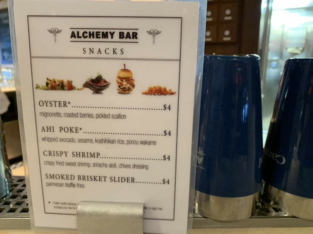 The menu at Alchemy Bar aboard the Carnival Vista cruise offers delectable snacks like oyster with mignonette, ahi poke with whipped avocado, crispy shrimp with aioli, and smoked brisket slider with fries. Each delicious option is paired perfectly with its price.