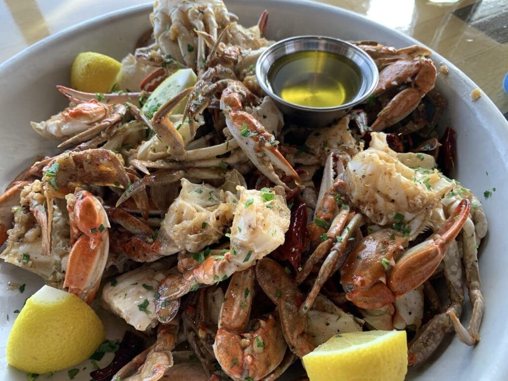 A large plate filled with cooked crab pieces, garnished with herbs and lemon wedges, reminiscent of a Carnival Vista cruise feast. A small metal dish containing melted butter is placed on top of the crabs, echoing the indulgence often highlighted in rave cruise reviews.