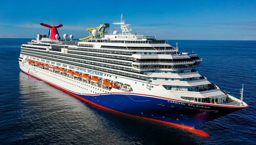 An exterior view of the Carnival Splendor, one of the renowned Carnival Cruise Line ships, sailing on calm waters under a clear blue sky. The large vessel boasts a distinctive red and white funnel, multiple decks with numerous windows and balconies. The ship's name is visible on the hull.