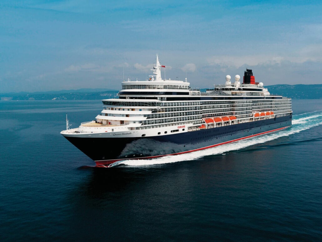 A large cruise ship, reminiscent of Cunard Ships, sails on a calm sea under a clear sky, with a distant coastline visible in the background.