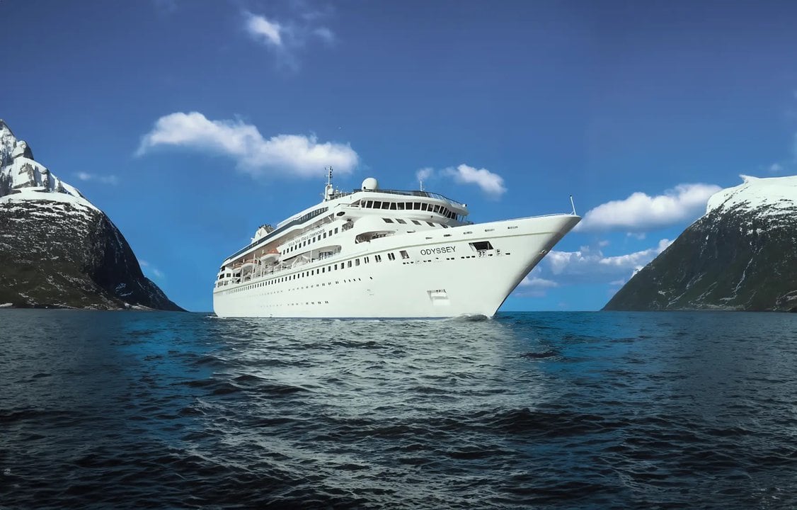 A WORLD CRUISE ship in the middle of the ocean with mountains in the background.