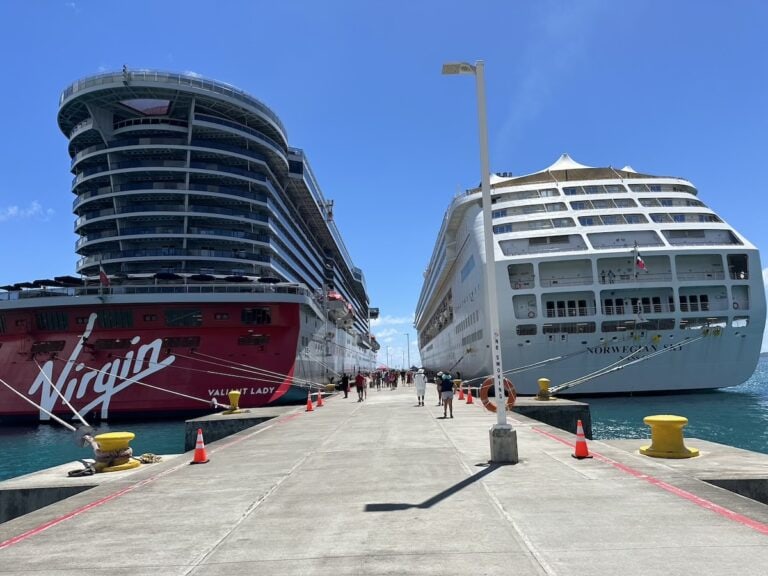 Two cruise ships docked at a port in the British Virgin Islands with passengers walking along the pier.