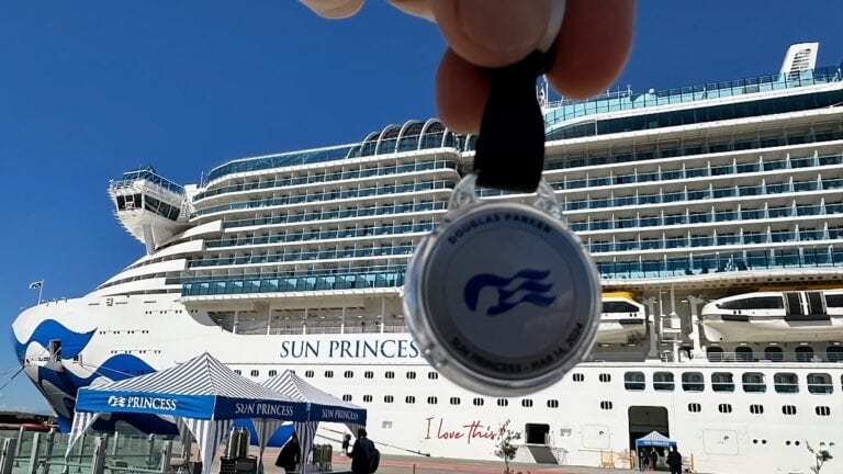 A medal with the Princess Cruises logo held up in front of the Sun Princess cruise ship during a review.