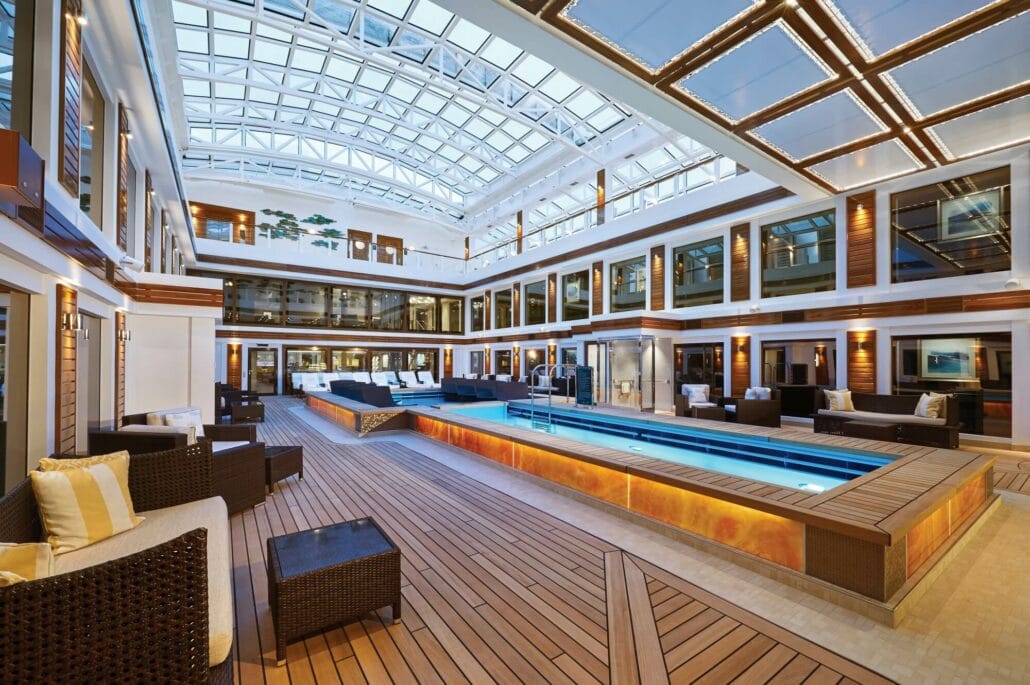 Norwegian Cruise Line ship atrium with a swimming pool and lounging areas under a glass canopy.