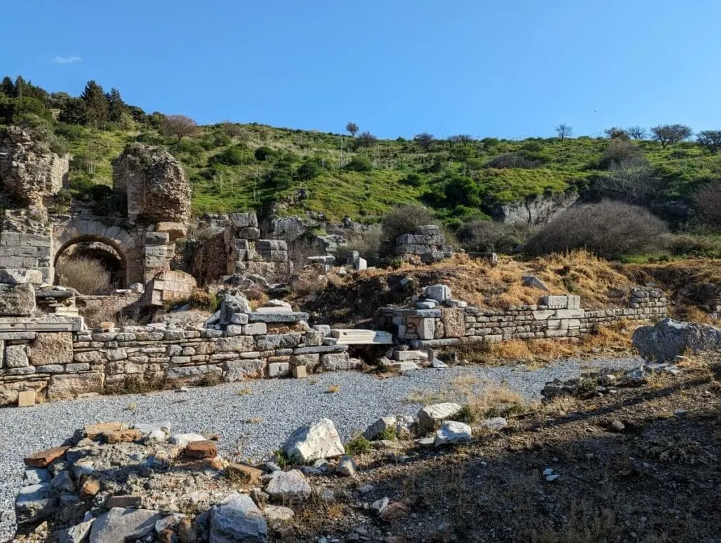 Ancient ruins with stone structures and arches amid greenery under a clear blue sky.