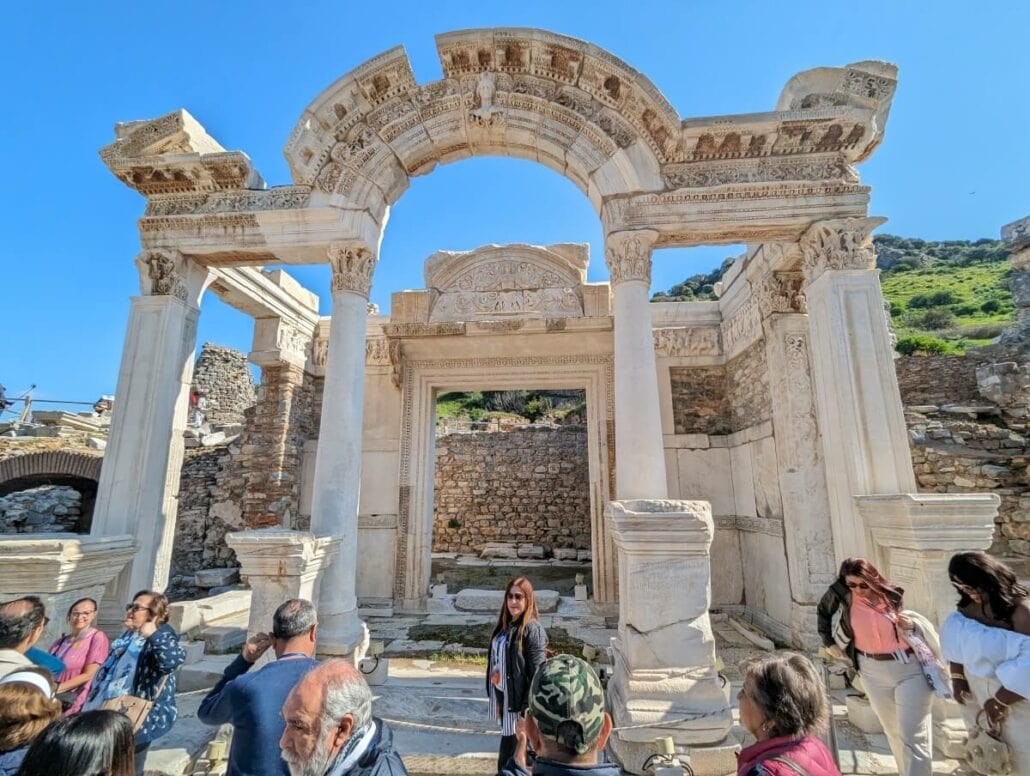 Visitors exploring the ruins of an ancient roman arch under a clear blue sky.