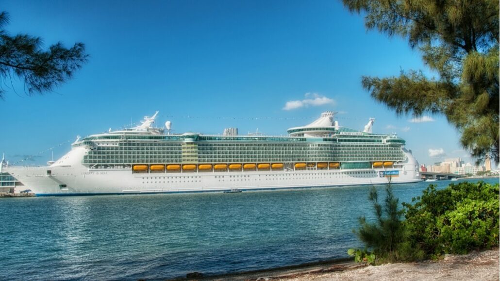 Large cruise ship docked near a coastline with trees.