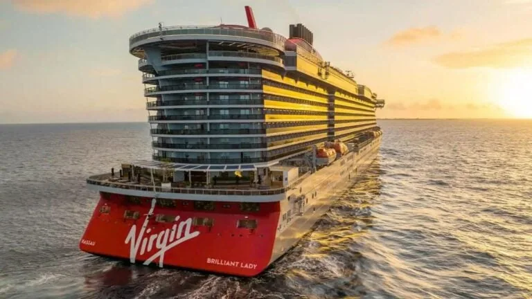 A large Virgin Ship Brilliant Lady, debuting in 2025, sailing on the ocean at sunset.