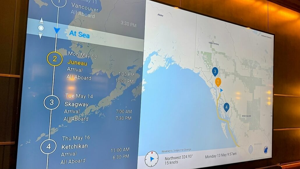 A digital screen display shows a cruise ship's itinerary for the Inside Passage in Alaska. The route includes stops in Juneau on May 13, Skagway on May 14, and Ketchikan on May 15, with details like arrival times and weather information included.