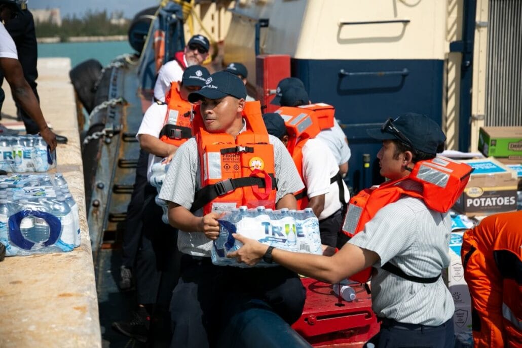 Emergency response team members in life vests unload water supplies from a Royal Caribbean ship onto a dock.