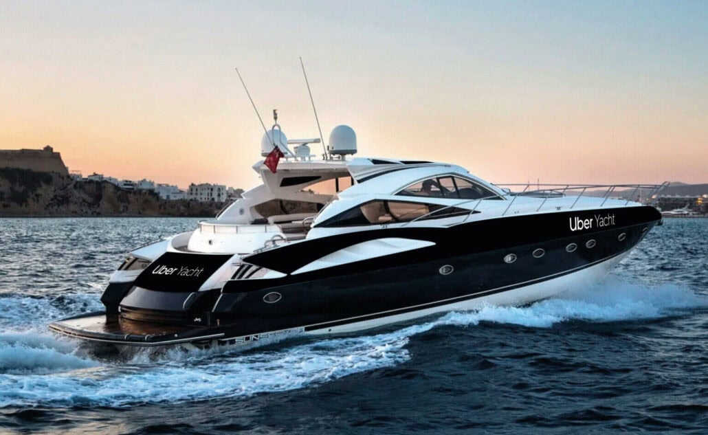 A sleek black and white yacht named "Uber Yacht" is cruising on the water at sunset, with a coastal town visible in the background, offering a taste of an elegant European Cruise Tour.