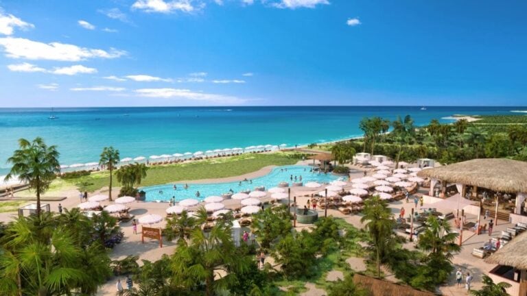 A scenic beachfront resort with sandy shores, tropical palm trees, a large pool surrounded by umbrellas and loungers, and clear turquoise waters under a blue sky features an exclusive Adults-Only Area perfect for relaxation.