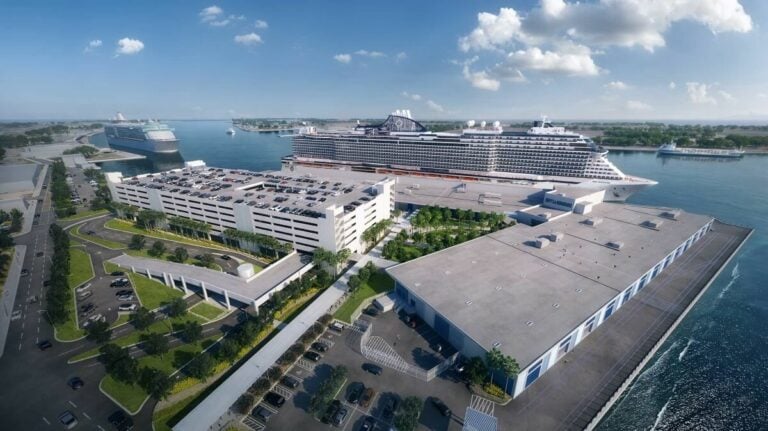 Aerial view of Galveston Port with two large cruise ships docked at the cruise terminal, a multi-level parking garage, and a nearby warehouse under a partly cloudy sky.