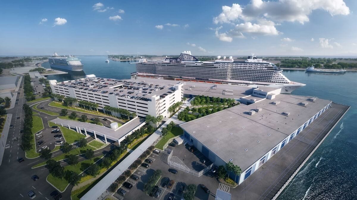Aerial view of Galveston Port with two large cruise ships docked at the cruise terminal, a multi-level parking garage, and a nearby warehouse under a partly cloudy sky.