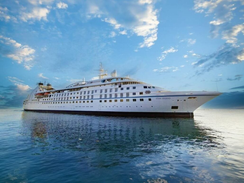 The Star Legend, a large white cruise ship from Windstar, is docked on calm water under a partly cloudy sky.