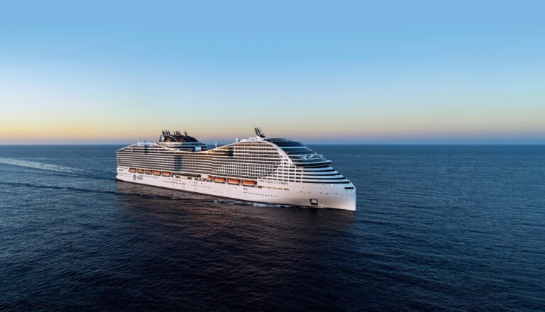 A large white cruise ship, MSC World America, sails on a calm ocean under a clear sky. The ship has multiple decks with lifeboats visible on the side. The horizon is visible, indicating the boat is traveling during either sunrise or sunset. Guests can enjoy Eataly at Sea's culinary delights onboard.