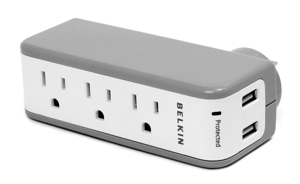 A white and gray Belkin surge protector with three AC outlets and two USB ports for charging devices. The word "protected" is printed near the USB ports. This compact, rectangular surge protector is perfect for travel, with plugs allowed onboard Royal Caribbean cruises.