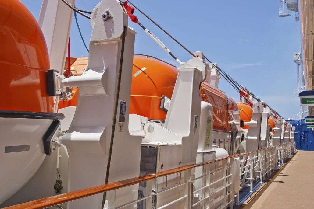 Row of orange lifeboats secured on the side of a cruise ship under a clear blue sky.
