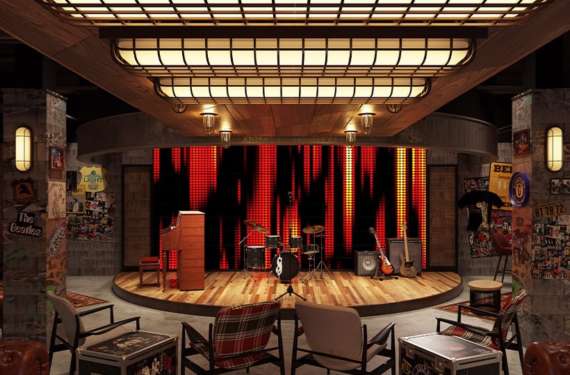 A cozy music venue with a wooden stage, drum set, and guitars. Red and black LED lights form the backdrop while the walls echo the Music of Prince. Various chairs face the stage, surrounded by posters and stickers.