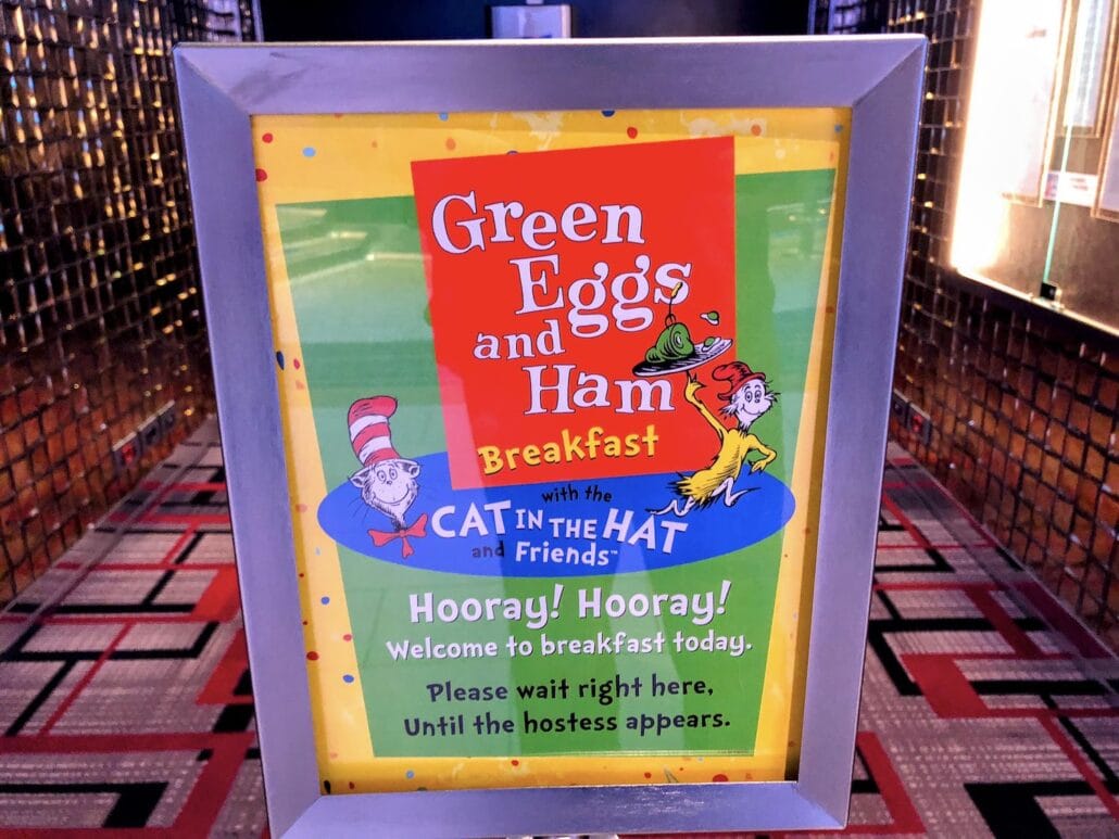 A framed sign whimsically advertises a "Green Eggs and Ham Breakfast with the Cat in the Hat and Friends" aboard Carnival Freedom. The text cheers, "Hooray! Hooray! Welcome to breakfast today. Please wait right here until the hostess appears," inviting guests to enjoy this colorful onboard treat.